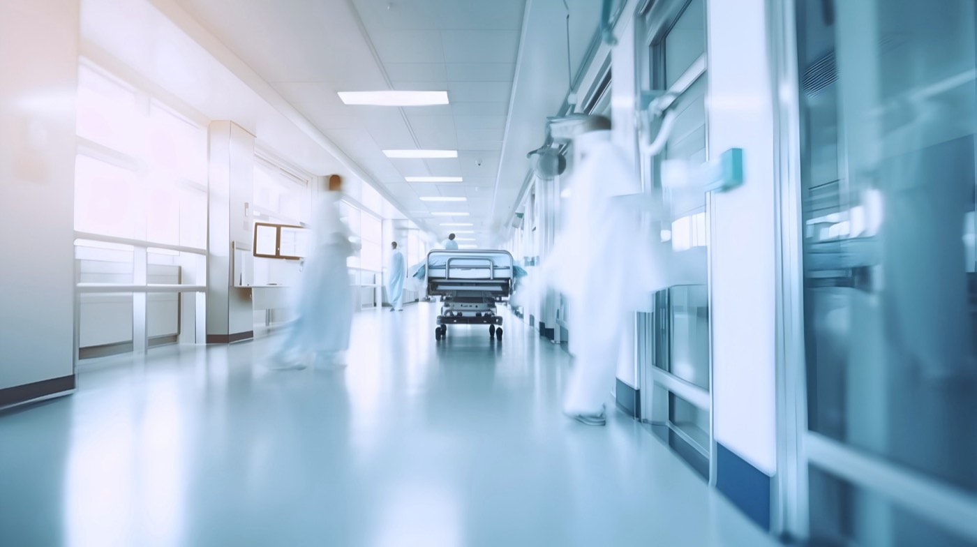 A bright hospital corridor with staff and a bed in motion