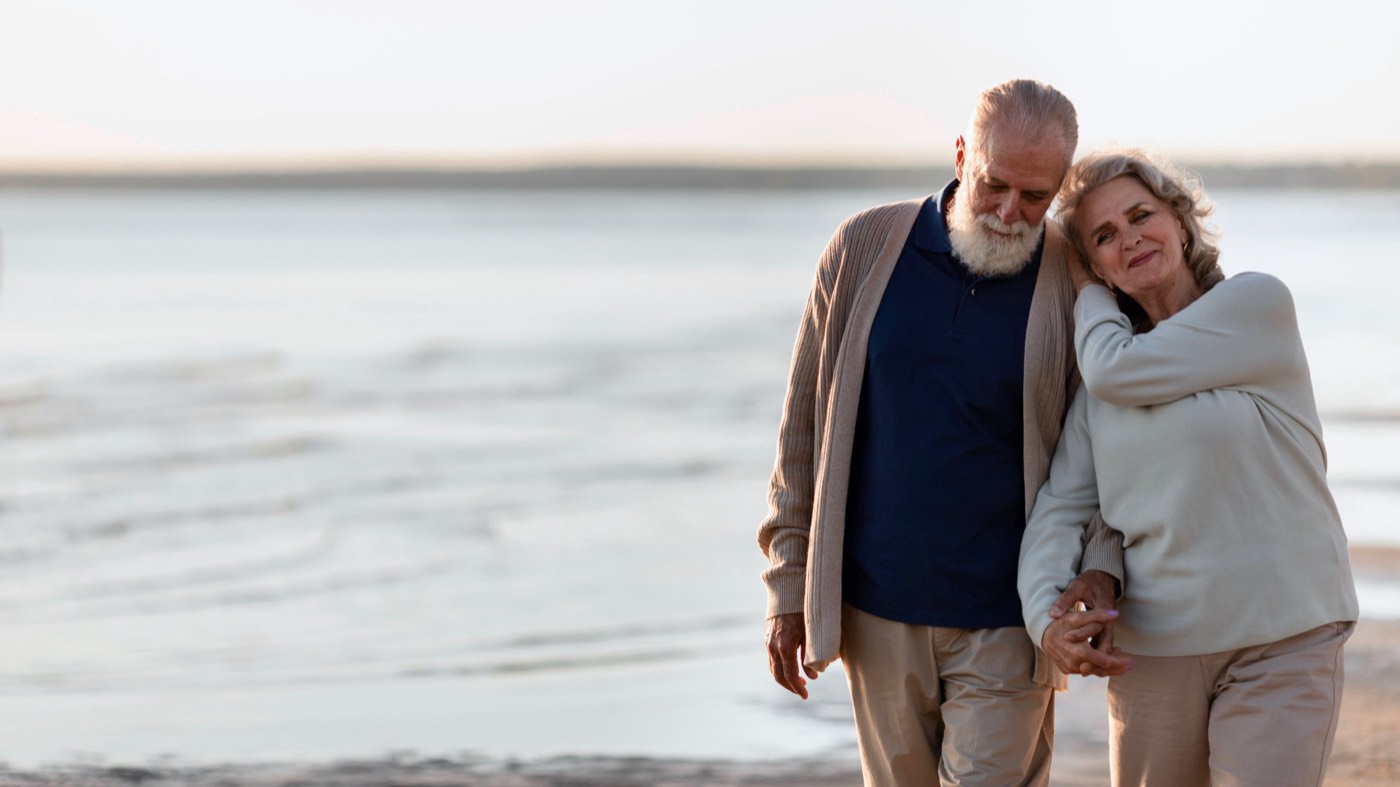 An older couple walking arm in arm along the beach